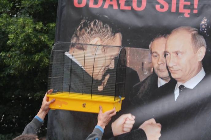 [Un manifestant présente une cage devant la photo de Donald Tusk, ici avec Vladimir Poutine]